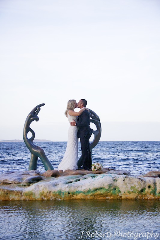 Couple kiss next to statues at Shelley Beach Rock Pool - wedding photography sydney